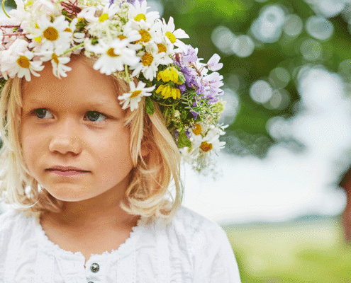 Glückliches blondes Mädchen mit Blumenkranz im weißen Hemd im Grünen