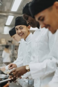 Strahlende Kochlehrlinge in weißer Kleidung bei der Arbeit